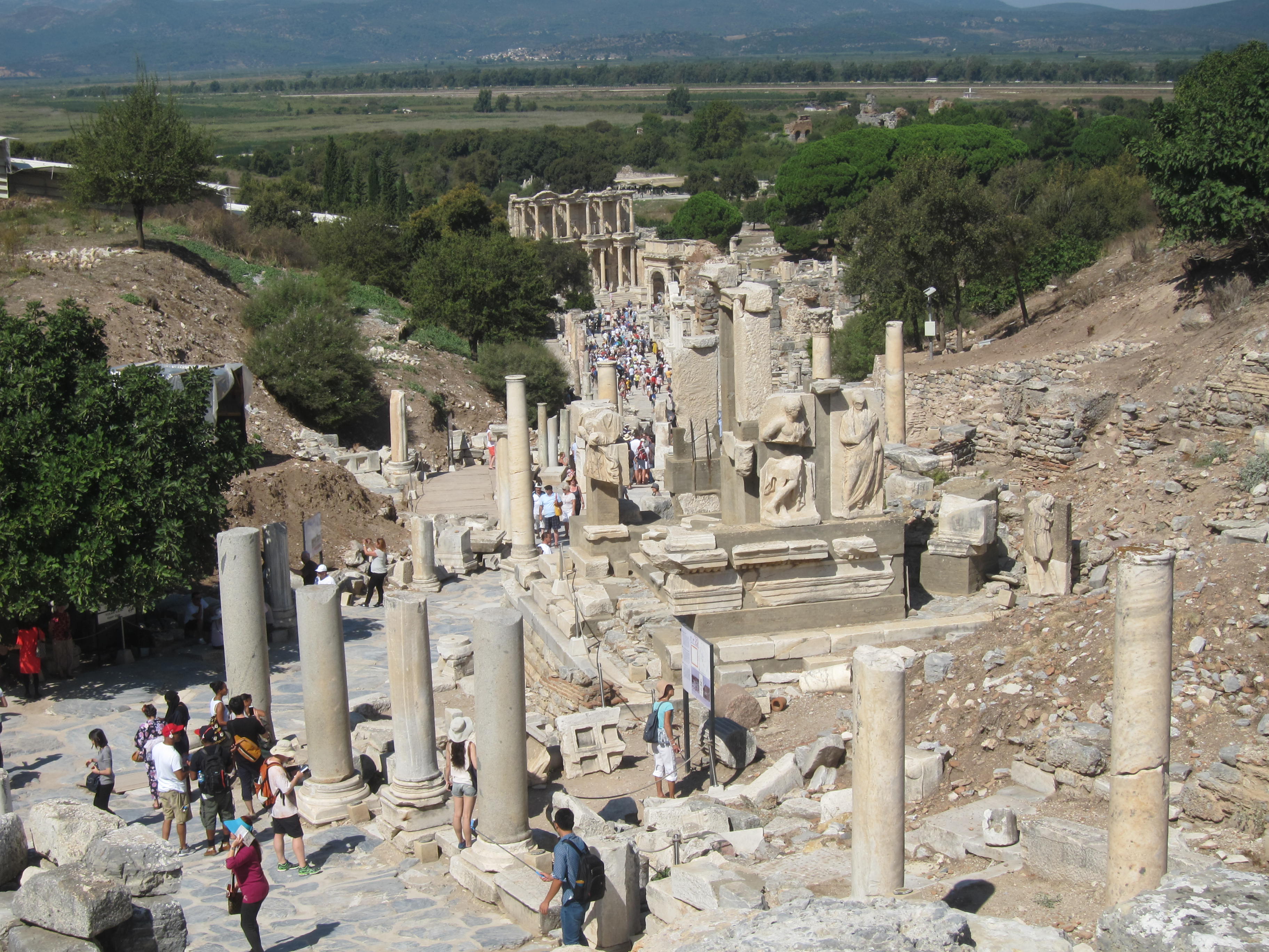Main road through Ephesus View of the Library of Celsus from the Upper Agora. The ancient
harbour would have been located beyond the archaeological site along the top of
the image. Carved reliefs are also visible at the centre right. Note the
crowds of people moving along the streets of the city centre.